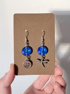 a pair of earrings with blue glass beads and silver metal buttons are displayed on a card