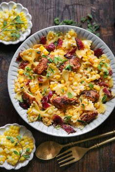 a white plate topped with pasta and meat next to corn on top of a wooden table