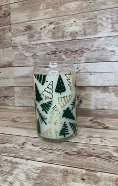 a white candle with green and gold christmas trees on it sitting on a wooden surface