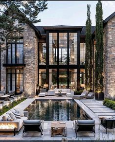 an outdoor swimming pool surrounded by lounge chairs and fire pit in front of a large stone building