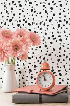 pink flowers are in a vase next to an alarm clock