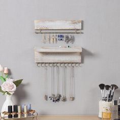 a wooden table topped with lots of jewelry next to a white vase filled with flowers