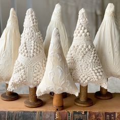 four white crocheted christmas trees sitting on top of a wooden table next to an old book