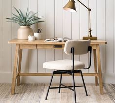 a desk with a chair, lamp and potted plant on it in front of a white wall