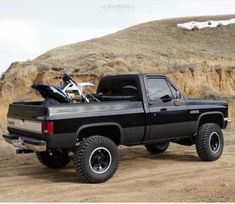 a black truck parked on top of a dirt road next to a mountain side with a motorcycle in the bed