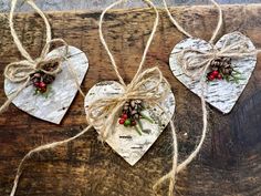 two wooden hearts with pine cones and berries tied to them on a piece of wood