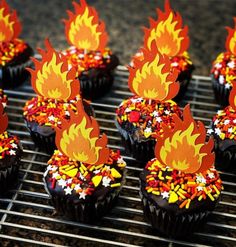 cupcakes decorated with fire and sprinkles on a cooling rack