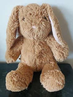 a brown stuffed rabbit sitting on top of a black table next to a white wall