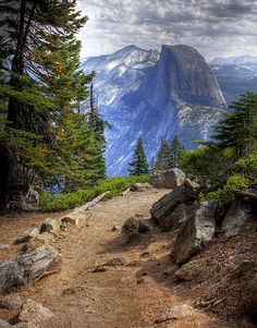 a path leading to the top of a mountain with trees on both sides and mountains in the background