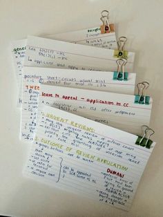 five pieces of paper with writing attached to clips on a white surface, all lined up and pinned together