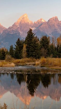 a mountain range is reflected in the still water of a lake with trees around it