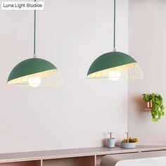 two green lamps hanging from the ceiling in a room with white walls and wooden furniture