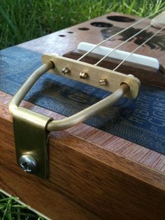 a close up of a wooden guitar case on the ground with grass in the background