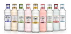 six bottles of london tonic water lined up on a white surface with one bottle in the foreground