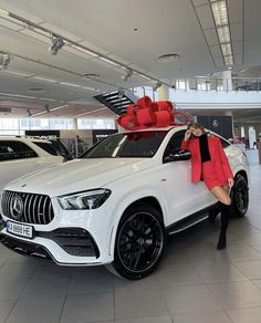 a woman leaning on the hood of a white mercedes suv in a showroom with red bows