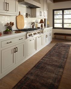 a kitchen with white cabinets and wood flooring next to a large rug on the floor