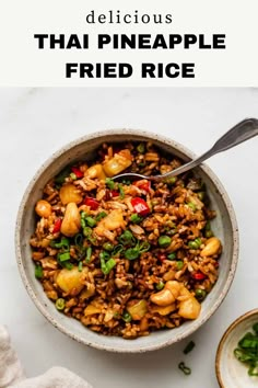 a bowl filled with fried rice and vegetables on top of a white table next to a spoon