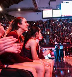 two women sitting on the sidelines at a basketball game and clapping to each other