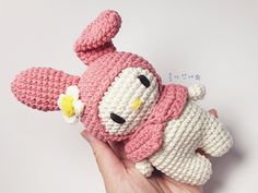 a hand holding a pink and white crocheted stuffed animal with a flower in its mouth