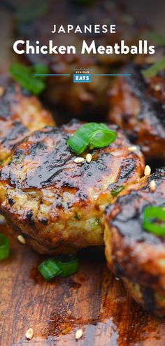 some meatballs are sitting on a wooden cutting board with green leaves and sesame seeds