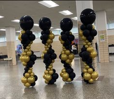 three tall black and gold balloons are in the middle of a floored area,