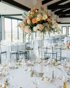 a tall vase filled with lots of flowers on top of a white table covered in glasses