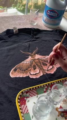 a person is painting a butterfly on a t - shirt with water glasses and a paintbrush