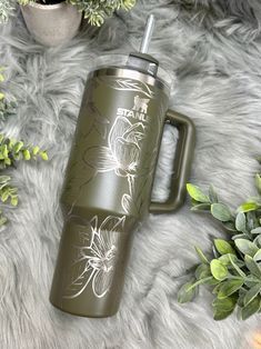 a green travel mug sitting on top of a fur covered floor next to potted plants