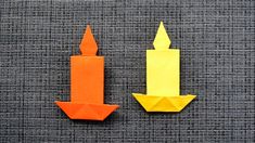 two orange and yellow candles sitting next to each other on top of a gray surface