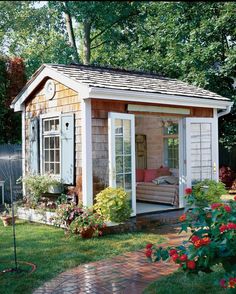 a small garden shed in the middle of a yard with flowers and plants around it