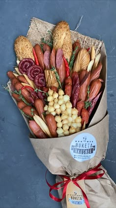 a bouquet of assorted meats and vegetables wrapped in brown paper with a red ribbon