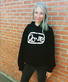 a woman standing in front of a brick wall wearing a black hoodie with the word gyr written on it