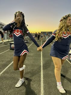 two cheerleaders holding hands while walking across a parking lot