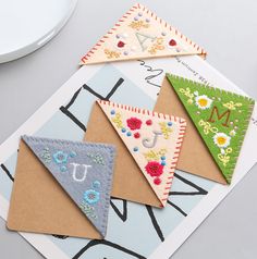 four different colored felt pennants sitting on top of a piece of paper next to each other