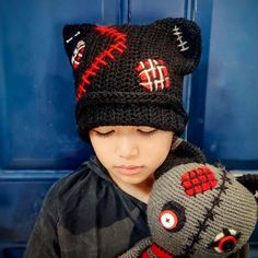 a young boy wearing a knitted hat and holding a stuffed animal in front of a blue door