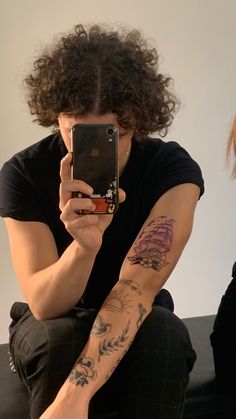 a man with long curly hair sitting down and holding a cell phone in his hand