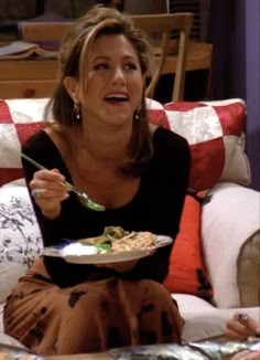 a woman sitting on a couch with a plate of food in her hand and looking up at the camera