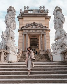 a woman is standing on the steps in front of a building with statues around her