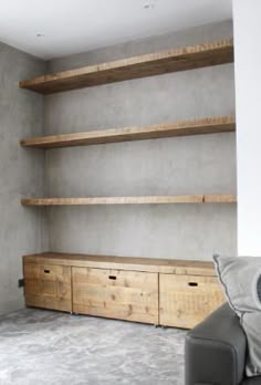 a living room with some shelves and a couch in front of the wall that is made out of concrete