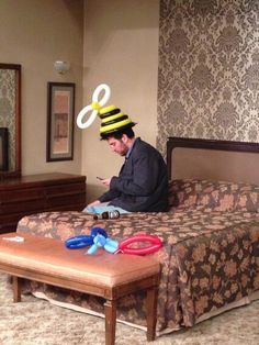 a man sitting on top of a bed wearing a hat with scissors and hair clips