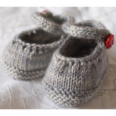 a pair of gray knitted baby shoes sitting on top of a white bed sheet