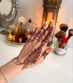 a woman's hand with henna on it and makeup brushes in the background