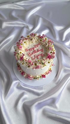 a white cake with pink and yellow sprinkles sitting on top of a white plate