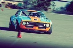 an orange and blue car driving down a race track in front of a cone on the ground