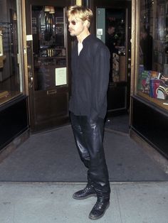 a man in black shirt and leather pants walking out of a building with his hands in his pockets