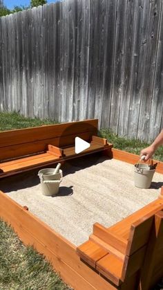 a person standing in front of a wooden bed with sand and buckets on it