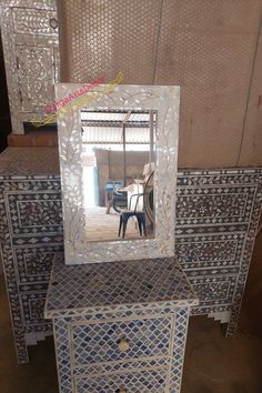 a mirror sitting on top of a white dresser next to a wooden table with drawers