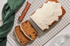 two slices of banana bread with icing on a cooling rack next to a knife and fork