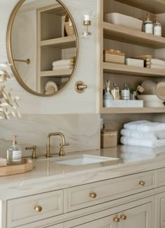 a white bathroom with gold accents and marble counter tops, along with shelves filled with folded towels