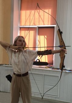 a woman holding a bow and arrow in front of a window